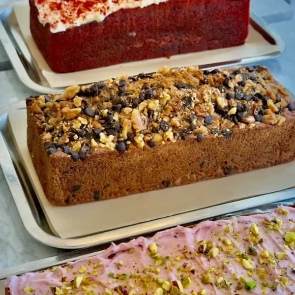 Tres bandejas apiladas con un bizcocho red velvet, un plum cake de nueces y chocolate y otro con glaseado rosa y pistacho picado