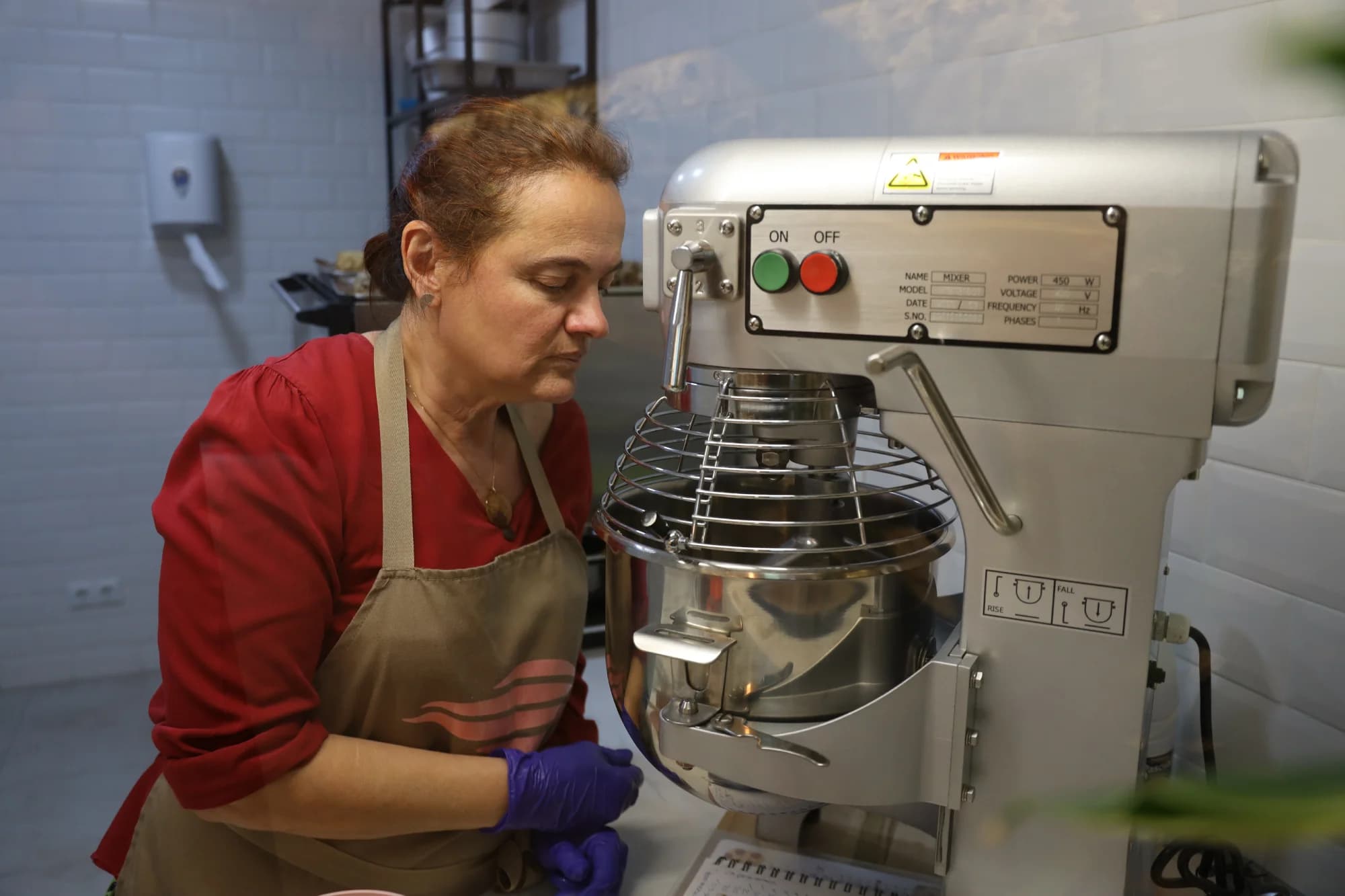 Repostera de Delicati con camisa granate y delantal trabajando de pie junto a la amasadora industrial del obrador