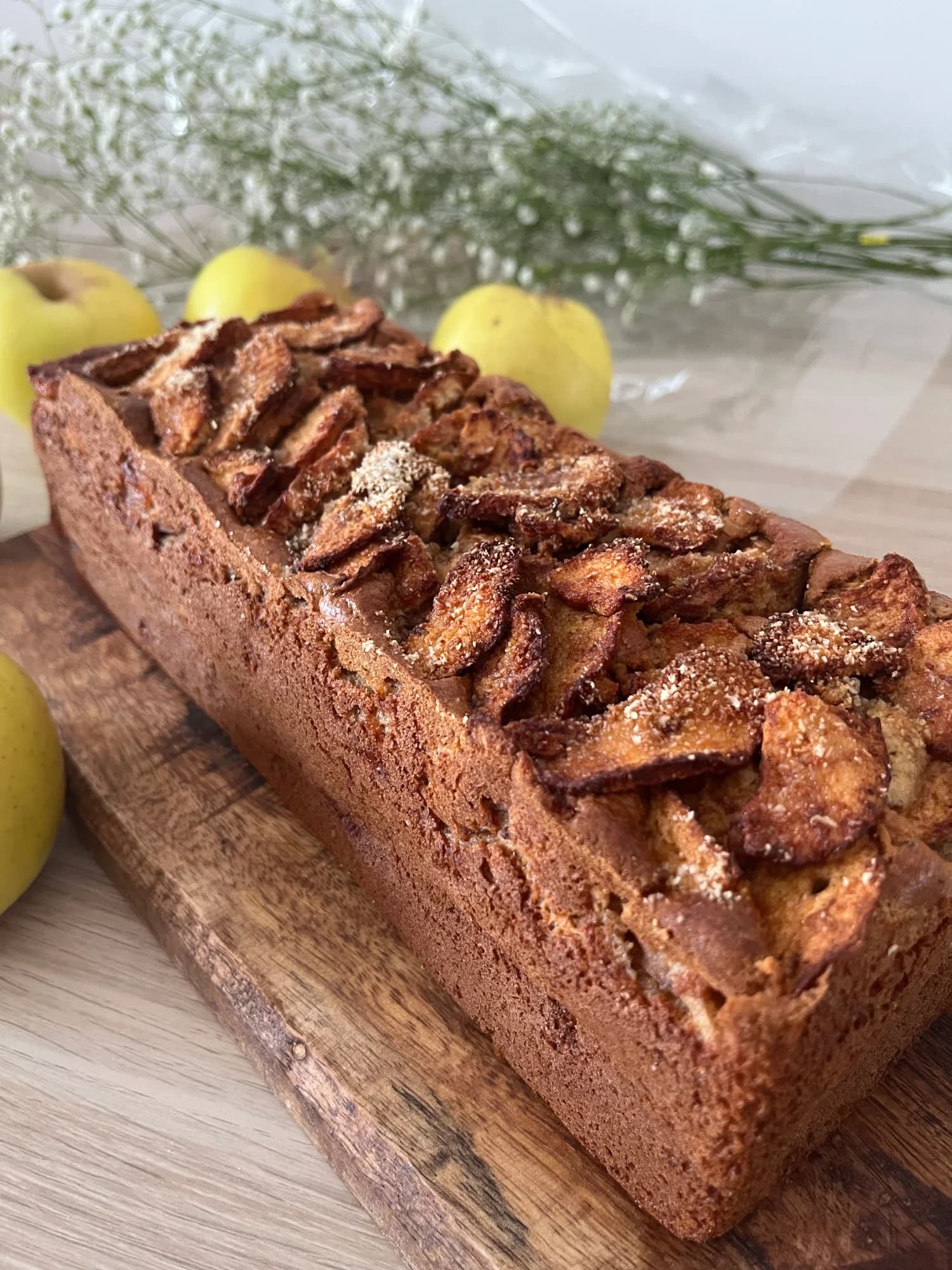 Plum cake de manzana con láminas de manzana caramelizada y azúcar espolvoreado cubriendo toda la superficie, sobre tabla de madera rústica
