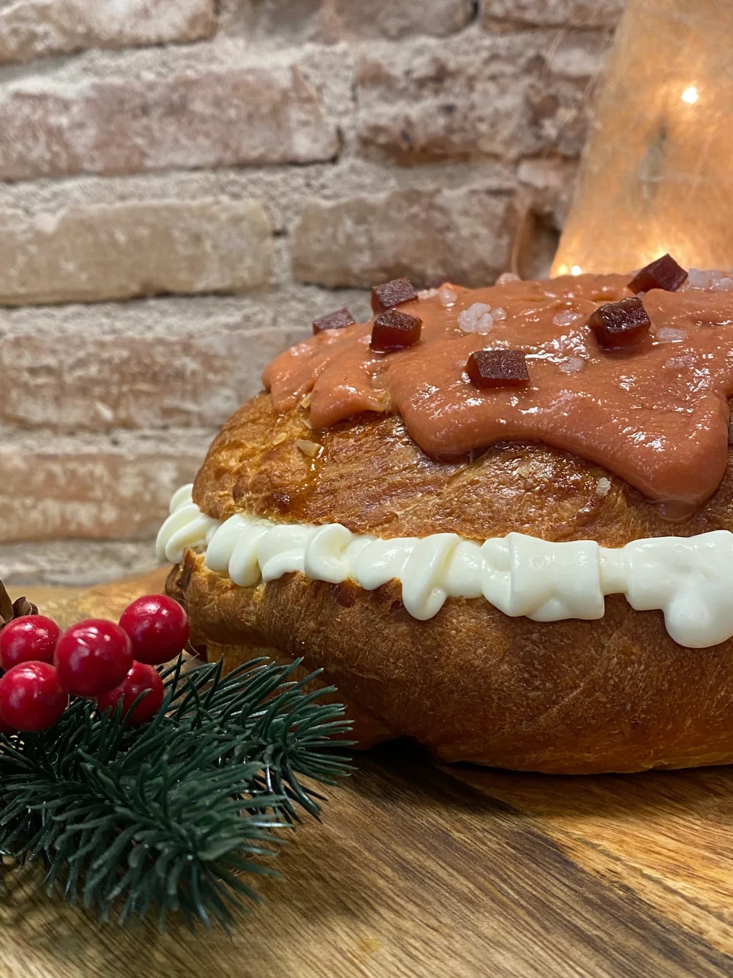 Roscón artesano relleno y cubierto de crema de turrón con dados de turrón por encima, decorado con acebo, sobre tabla de madera y pared de ladrillo