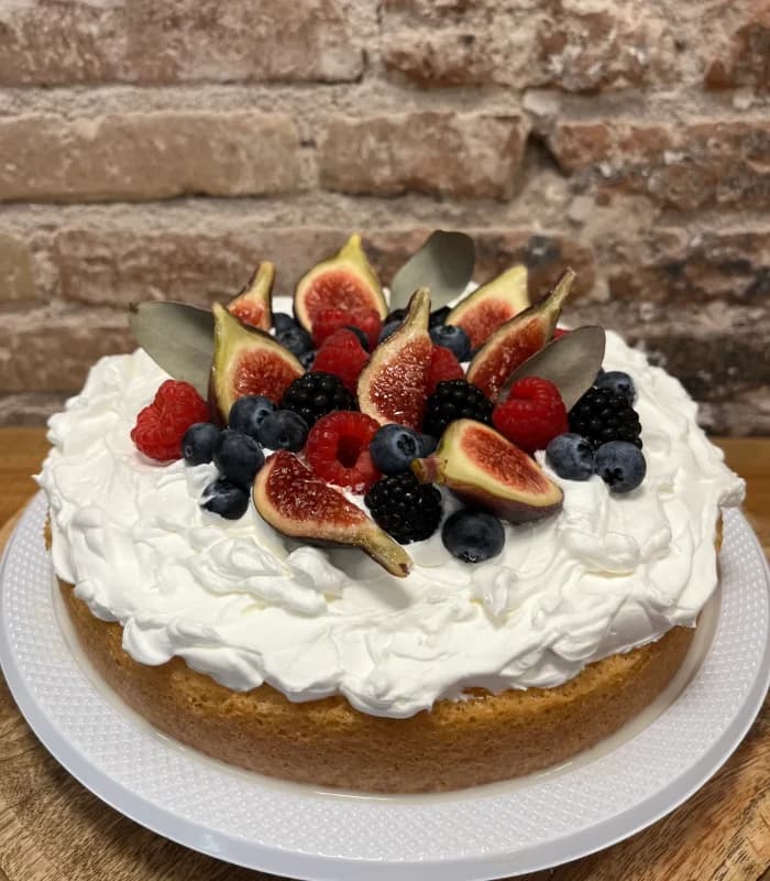 Tarta redonda cubierta de nata montada y coronada con higos abiertos, frambuesas, moras y arándanos frescos, sobre plato blanco