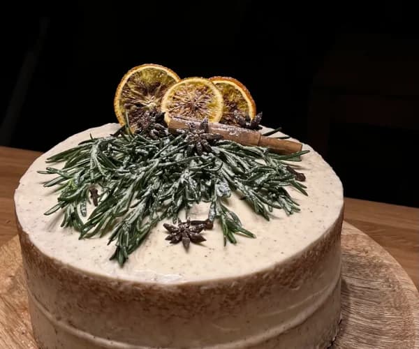 Tarta redonda con cobertura lisa decorada con ramas de romero escarchado, rodajas de naranja deshidratada, canela en rama y anís estrellado